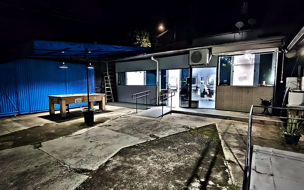 A fachada da barbearia à noite, com o pátio na frente