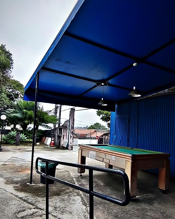 O pátio coberto por uma tenda azul, com a mesa de sinuca e o corrimão